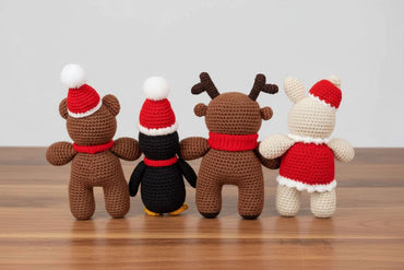 Four crochet toys with Santa hats on a wooden surface.