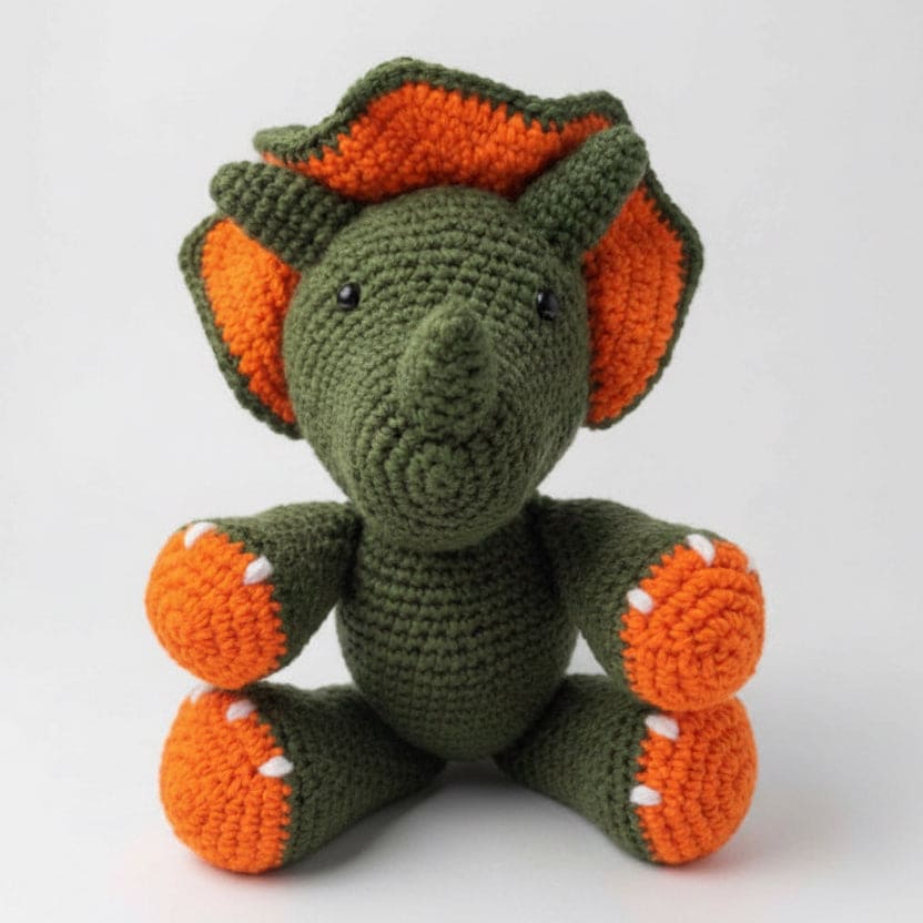 Crocheted dinosaur toy with green body and orange spikes on a white background