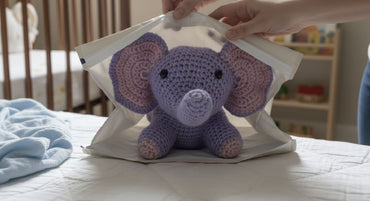 Purple crochet elephant toy inside a clear plastic bag on a bed.