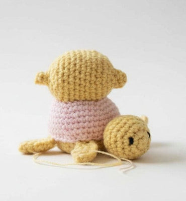 Crocheted toy resembling a turtle with a pink shell on a light gray background