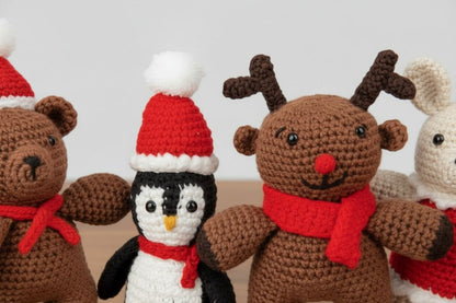"Four crocheted Christmas toys: reindeer, penguin, bunny, and bear with scarves and hats."