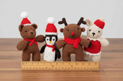 Four crocheted Christmas-themed animals with a ruler for scale on a wooden surface.