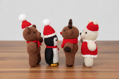 Four crochet animals wearing Christmas hats and scarves on a wooden surface.