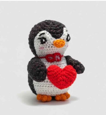 Crocheted penguin holding a red heart on a white background