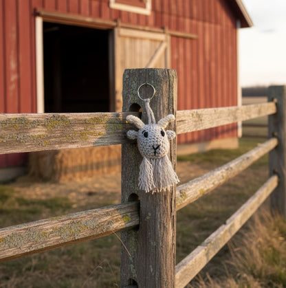 Goat keychain hanging on a wooden fence with a red barn in the background
