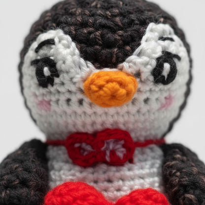 Close-up of a crocheted penguin with a red bow tie on a white background