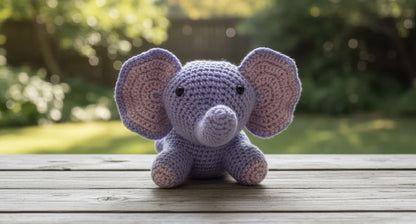 Crocheted purple elephant toy on a wooden surface with a blurred natural background