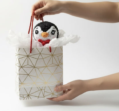 Handmade crochet penguin toy being placed into a gift bag with geometric pattern
