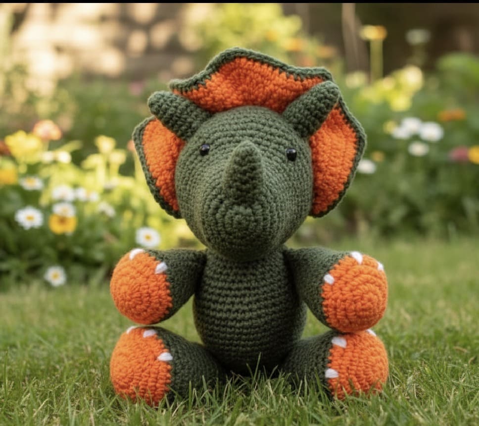  "Green and orange crocheted dinosaur toy on grass with flowers." 