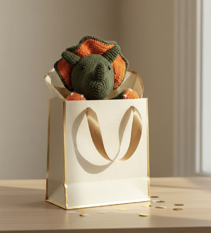 Crochet dinosaur toy in a gold gift bag on a wooden surface with a neutral background
