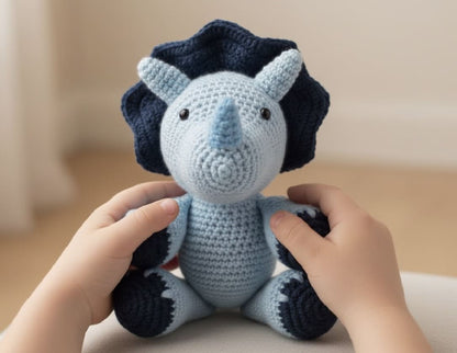 Handmade crochet dinosaur toy held by two hands against a neutral background