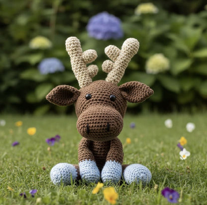 Crocheted moose toy on grass with flowers in the background