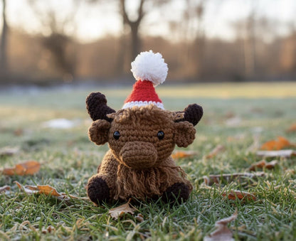 Crocheted cow toy wearing a Santa hat on a grassy field with a blurred background