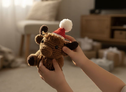 Hand holding a small brown plush toy with a red and white hat in a cozy indoor setting.