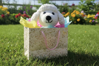 White dog plush toy in a decorative paper bag on grass with flowers in the background