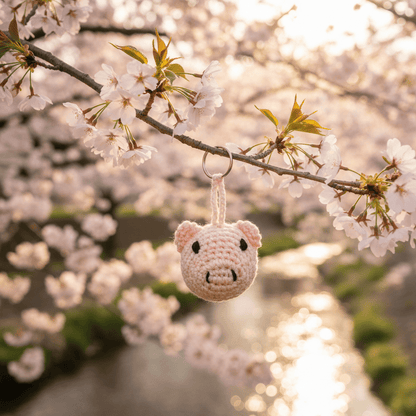 Crocheted pig keychain hanging from a cherry blossom branch