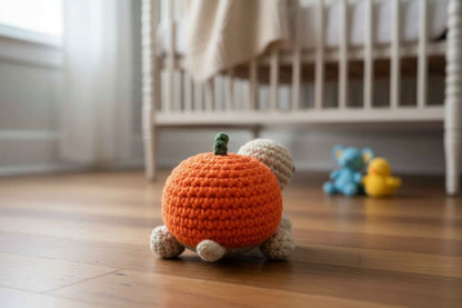 Crocheted pumpkin toy on a wooden floor with a crib in the background