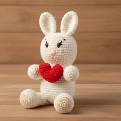 Crocheted bunny holding a red heart on a wooden surface